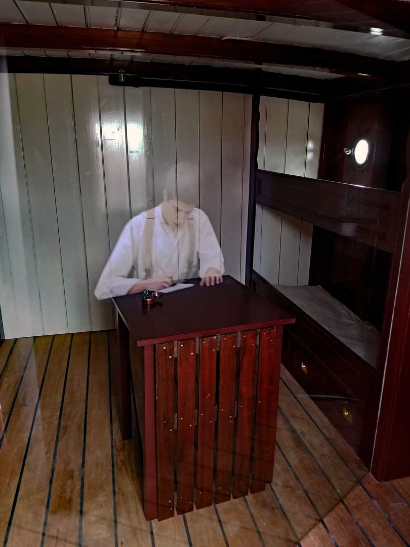 An image from a cabin with a hologram of a young sailor writing a letter, to home maybe...